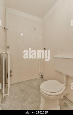 a bathroom with white tiles on the walls, and a toilet in the middle part of the room is empty Stock Photo
