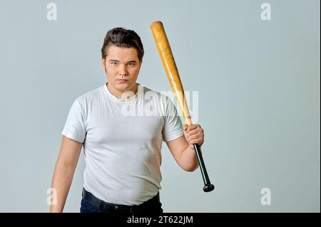 A man with a bat in his hands swings on a gray background Stock Photo