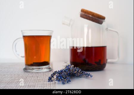 Blured black tea in a glass cup and glass teapot on a napkin and lavender on white table with white background Stock Photo