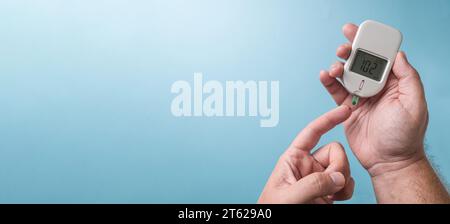 Man measuring blood sugar level with a glucometer. Diabetes concept on blue background Stock Photo