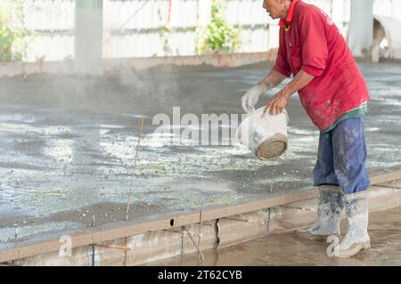 Worker scatter cement powder on surface of wet concrete insert Metal net on Floor in building site. Stock Photo