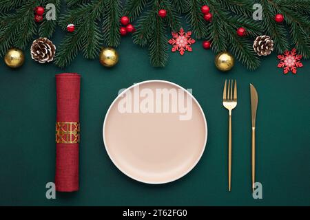 Clean empty plate, golden cutlery. Festive table setting with christmas decorations. Celebration xmas eve, flat lay. Red, gold and green accents. Fir Stock Photo