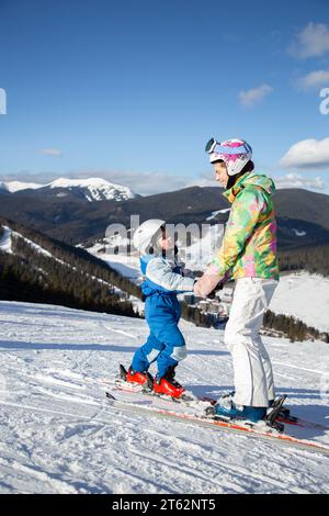 preschool boy and teenage girl stand on a mountain slope on skis holding hands. Ski lessons for children. Winter sports for the family. Frosty sunny w Stock Photo