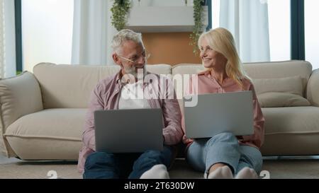 Successful happy mature caucasian married couple man woman entrepreneurs grandfather grandmother using laptops computer remote work on Internet Stock Photo