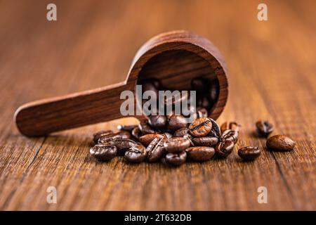 Roasted coffee beans in wooden scoop on the wooden table. Stock Photo