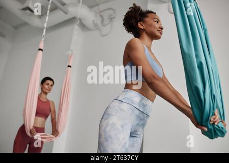 Side view portrait of African American young woman holding hammock while practicing aerial yoga in studio Stock Photo