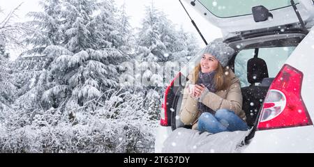 Woman in woolen hat sits in the trunk of the car and holds a cup of hot tea in her hands.. Stock Photo