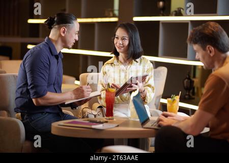 Cheerful business colleagues discussing ideas for project development when meeting in hotel lounge area Stock Photo