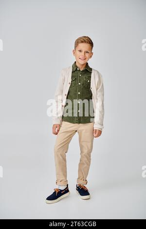 vertical shot of preadolescent boy in stylish outfit smiling at camera on gray backdrop, fashion Stock Photo