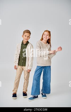 cheerful preadolescent children in stylish casual clothes posing on gray backdrop, smiling at camera Stock Photo