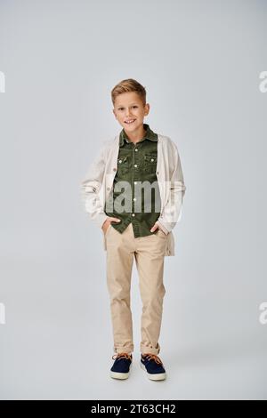 vertical shot of preteen little boy in casual outfit on gray backdrop with hands in pockets, fashion Stock Photo