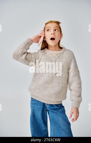 amazed little girl in stylish casual attire talking by phone and looking away, fashion concept Stock Photo