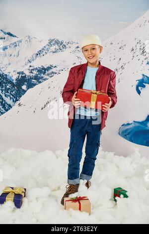 vertical shot of cheerful little boy in red jacket holding present and smiling at camera, fashion Stock Photo