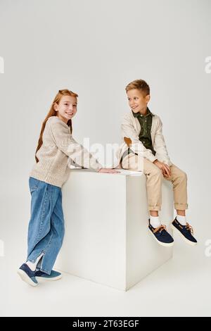 cheerful little boy in cardigan smiling at preteen red haired girl that looking at camera, fashion Stock Photo