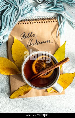 Top view of cup spiced tea with cinnamon sticks and dried orange slices, surrounded by vibrant yellow autumn leaves are juxtaposed against a notebook Stock Photo