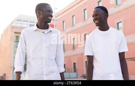 Happy two African American young men sharing a light moment against an urban backdrop looking at each other Stock Photo