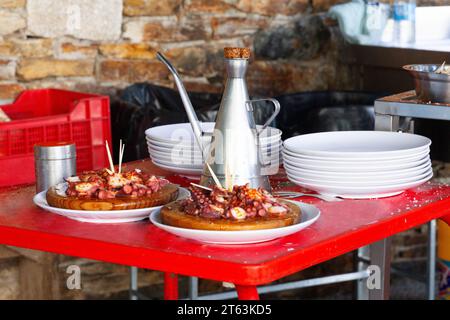 Grilled octopus delicacies presented on wooden plates accompanied by an elegant metal pitcher, stacked white dishes, and cooking tools, arranged on a Stock Photo