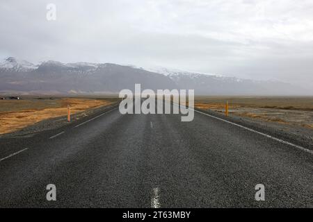 Asphalt empty roadway with markings running through field leading towards snow covered mountains in Iceland Stock Photo