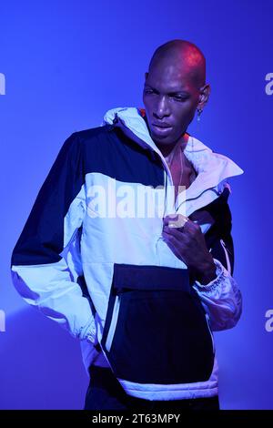 Stylish confident bald young man in casual outfit looking down and posing on blue background with hand in pocket Stock Photo