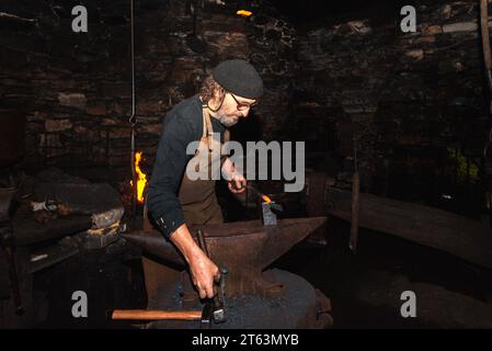 A blacksmith works meticulously, forging an 18th century hydraulic mallet using traditional methods, this rare object is among the last of its kind in Stock Photo