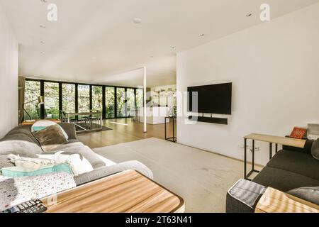 Comfortable sofa with wooden table and television on white wall against large window in spacious white living room at home Stock Photo