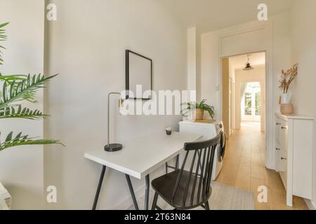 Lamp with coffee cup on desk and empty chair by washing machine in home office at contemporary white apartment Stock Photo