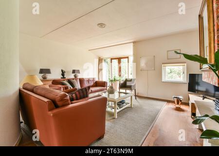 Brown leather sofa and coffee table placed in front of television against large window in white living room at modern apartment Stock Photo