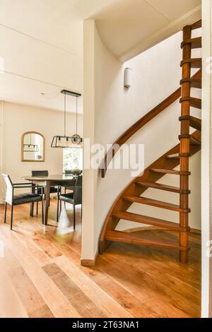 Wooden spiral staircase leading to second floor and dining table with chairs arranged in dining room at modern home Stock Photo