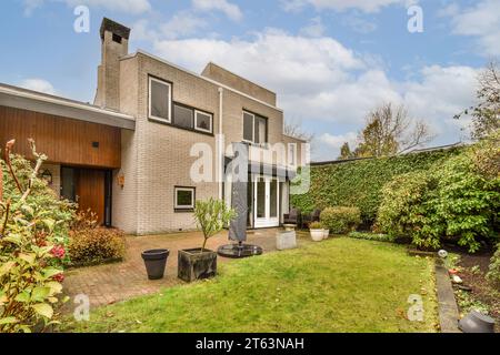 Grassy lawn with lush plants growing in backyard of modern brick house against cloudy sky in daytime Stock Photo