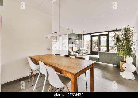 Wooden table with white chairs in spacious dining room of modern house with living room in background Stock Photo