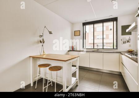 Wooden table and stools in spacious kitchen with white cabinets and bright window at contemporary house Stock Photo