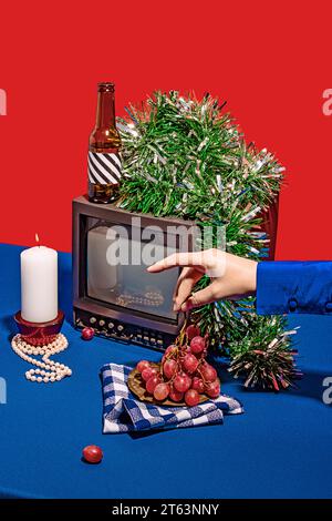 High angle of vintage television set surrounded by an array of different objects on blue table against red background, while a crop anonymous person p Stock Photo