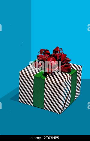 striped black and white gift box adorned with a shiny red bow and a green ribbon placed against blue background Stock Photo