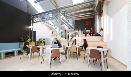 Busy coworking office in Madrid, Spain, showcasing professionals engaged in various activities the interior boasts an industrial design with plants, s Stock Photo