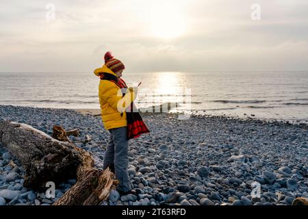 Woman in bright yellow jacket walking alone on the seaside on cold winter day. Travel  Lifestyle concept Stock Photo