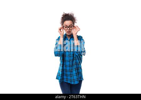 young joyful caucasian curly lady dressed in a plaid shirt adjusting her glasses Stock Photo