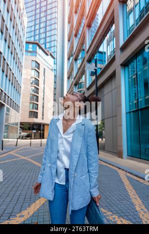 a woman in casual clothes walks around the city, lost among the skyscrapers Stock Photo