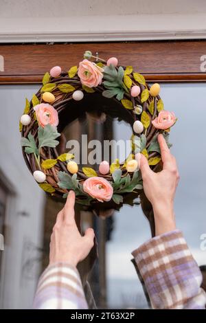 woman hanging a flower easter wreath on the door to the house Stock Photo