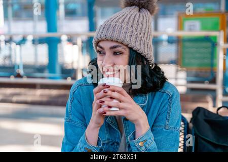 a young woman in a denim jacket is talking on the phone and waiting for a tram, bus at the stop Lifestyle photo Stock Photo
