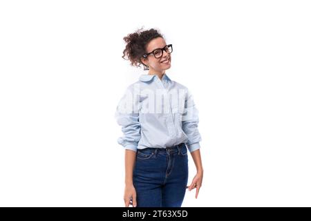 an amazing young brunette curly-haired manager woman is dressed in a loose-fitting light blue shirt tucked into jeans Stock Photo