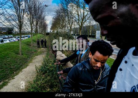 Michael Bunel/Le Pictorium - Exile in the land of human rights - 16/03/2018 - France/Ile-de-France (region)/Paris - Gathering in front of the Seine et Marne administrative detention center. Several people try to communicate with the detainees in the detention center under the eye of the police. In the background, a plane prepares to land at Roissy Charles de Gaulle airport. March 15, 2018. Le Mesnil Amelot. France. In October 2015, the municipality presented eighteen commitments in a document entitled 'Mobilizing the Paris community to welcome refugees'. The document opens with Stock Photo