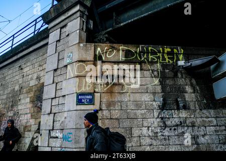 Michael Bunel/Le Pictorium - Exile in the land of human rights - 12/03/2018 - France/Ile-de-France (region)/Paris - A man passes under a graffiti calling for an end to the Dublin procedure at Porte de La Chapelle. The Dublin procedure obliges refugees and migrants to apply for asylum in the first country where their fingerprints have been registered. March 11, 2018. Paris. France. In October 2015, the municipality presented eighteen commitments in a document entitled 'Mobilizing the Paris community to welcome refugees'. The document opens with this sentence: 'Paris, like other Stock Photo