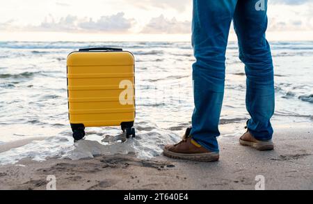 Man  with a yellow suitcase relaxing alone on the seaside at sunset.  Man waiting for a cruise ship   Travel  Lifestyle concept Stock Photo