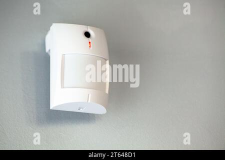 A white motion sensor camera on a gray wall, providing security and surveillance Stock Photo