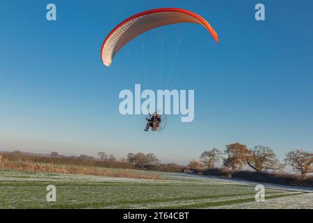 Para-Glider coming into land on a frosty and icy field with an orange sail Stock Photo