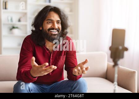 Indian guy vlogger streaming from home, using phone on tripod Stock Photo
