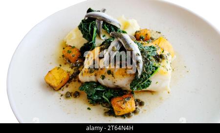 Cooked fillet of cod with anchovies served with cabbage, potato, carrots and capers - John Gollop Stock Photo