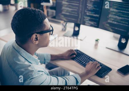 Back rear view photo of young man sit table working remote using his computer typing keyboard rewrite code indoors inside home workspace Stock Photo