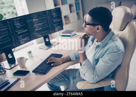 Side photo of male programmer student thinking how fix bugs error in code typing keyboard browsing his perfect html css job at workspace Stock Photo