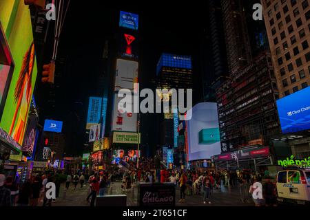 Manhattan skyscrapers come to life at night, with vibrant LED billboards lighting up Broadway and crowds of people bustling around iconic red stairs i Stock Photo